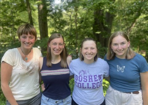 four young adult women posing in front of a green leafy background